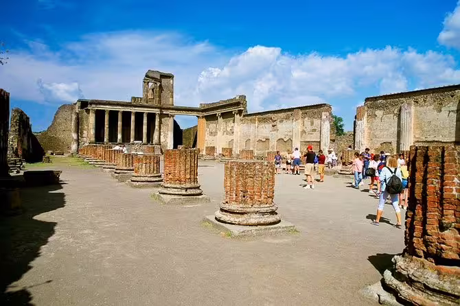 Group tour at Pompeii ruins from Naples, walking among ancient columns and courtyards under blue sky
