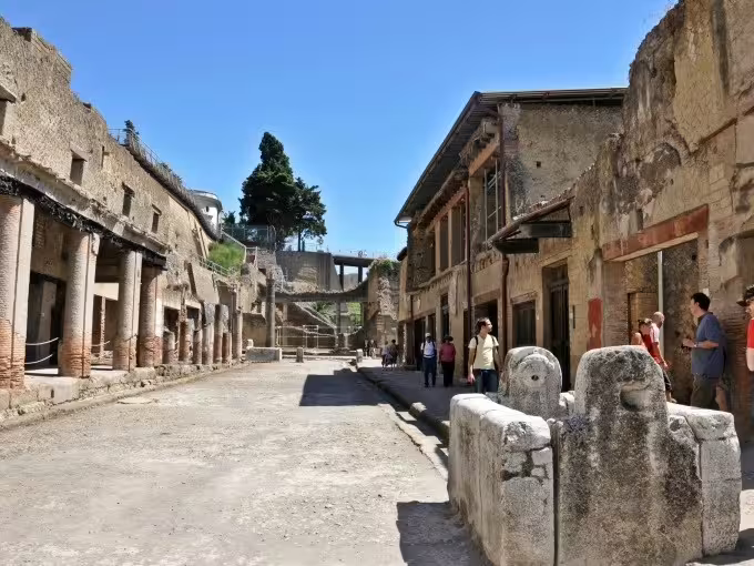 Pompeii ruins street scene on Naples group tour, ancient Roman buildings and visitors under blue sky