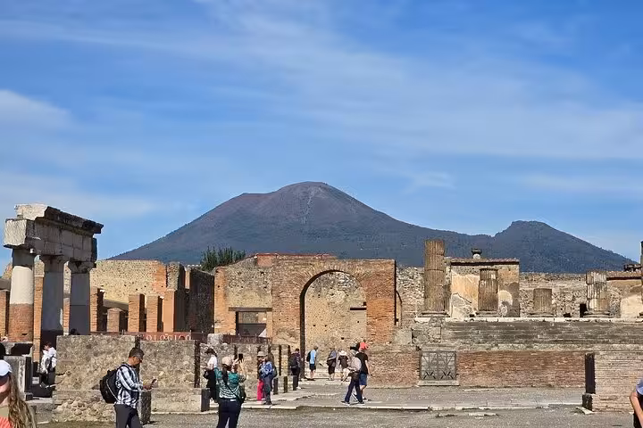 Tourists explore ancient ruins with Mount Vesuvius looming in the background, showcasing Pompeii's historical allure.