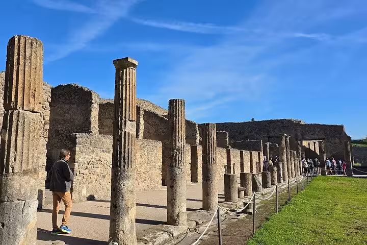 Visitors exploring Pompeii's preserved ruins and columns under a clear blue sky, highlighting historical significance.