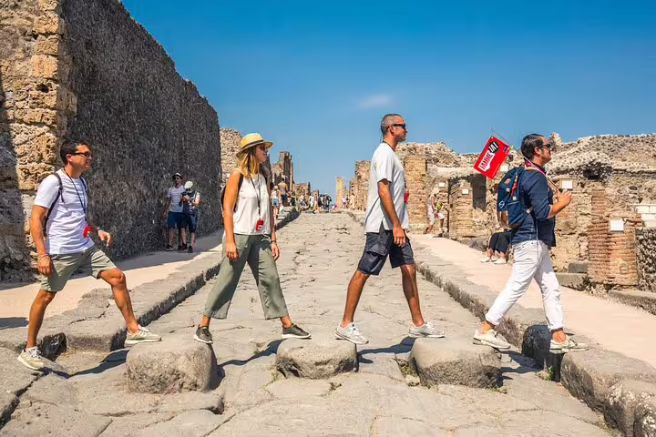 Tourists exploring ancient stone streets of Pompeii on a sunny day with ruins in the background on a Naples day trip.