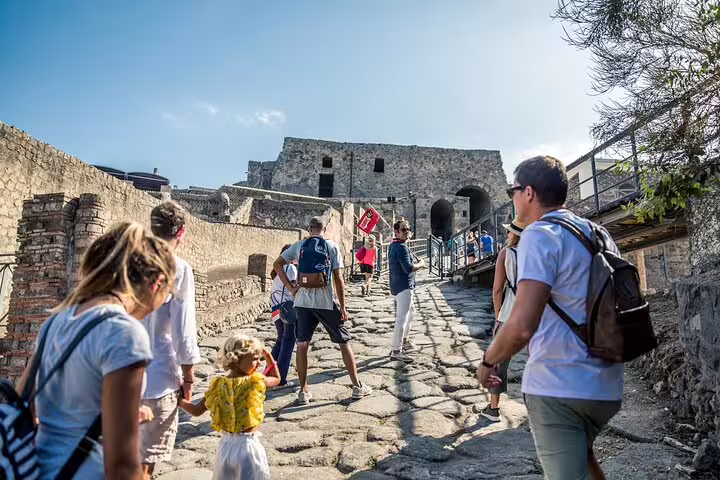 Visitors climbing cobblestone paths towards historic structures in Pompeii under a clear sky on a guided Naples excursion.