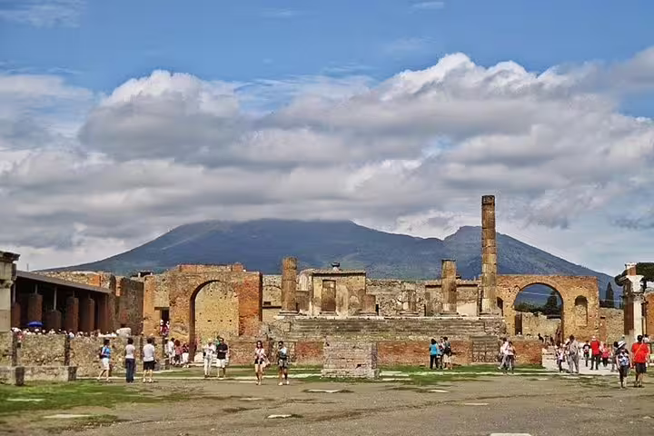 Guided group exploring Pompeii ruins with Mt Vesuvius in the background on a shared tour from Naples with winery visit