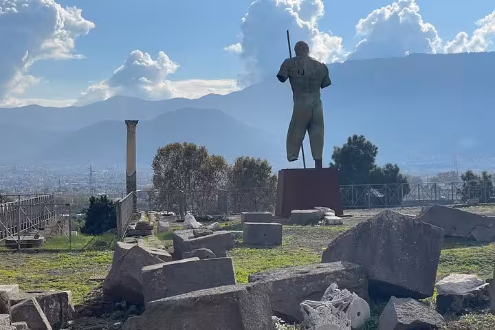 Statue and ancient ruins at Pompeii with scenic mountain views, included in a private skip-the-line access tour.