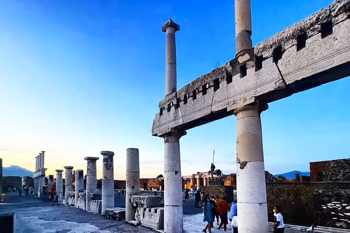 Tourists exploring the iconic columns and ruins of Pompeii under a clear blue sky during a private tour.