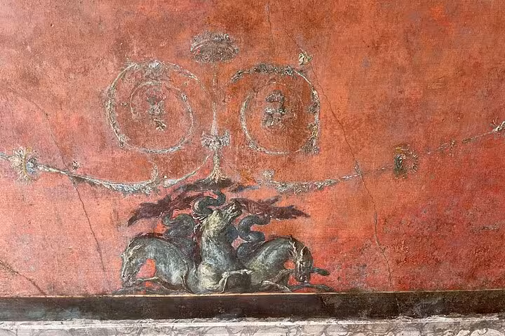 Detailed red fresco in Pompeii featuring mythical creatures and ornate designs, illustrating Roman artistic mastery.