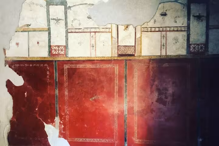 Colorful fresco with red and white panels, showcasing Roman artistry in Pompeii on an archaeological guided tour.
