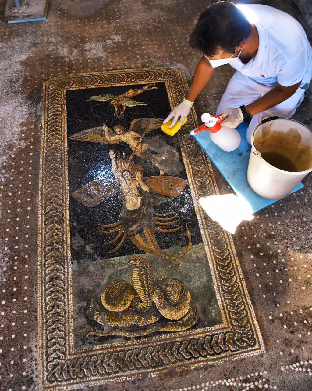 Conservator cleaning Roman mosaic at Pompeii on Naples group tour, archaeological visit with wine tasting