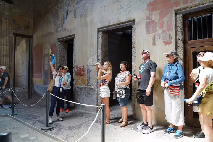 Tourists explore the ancient frescoes inside a preserved building at the Pompeii Ruins, capturing photos of historic artwork.