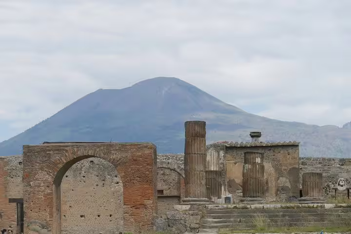 Pompeii archaeological site ruins with arch and columns under Mount Vesuvius, budget tour from Naples