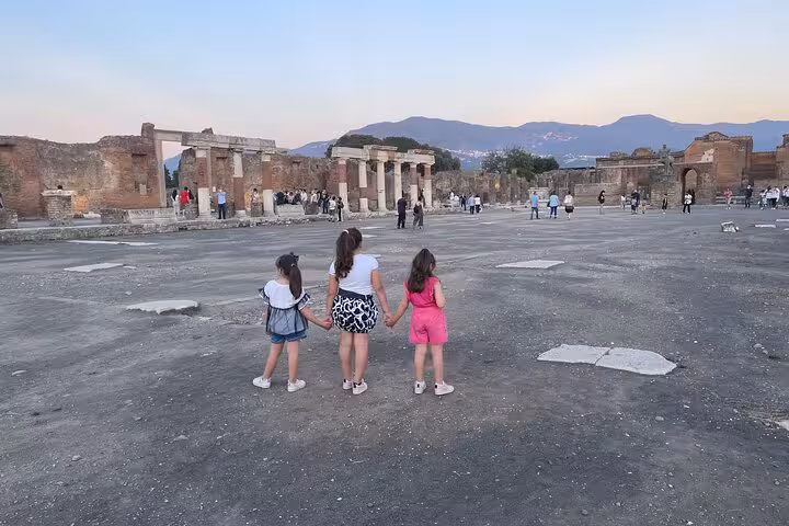 Children explore the vast ruins of Pompeii at dusk, surrounded by ancient architecture and scenic mountain views.
