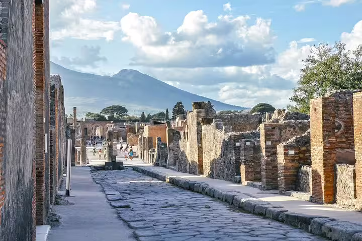 Ancient cobblestone street in Pompeii ruins with Mount Vesuvius view, low cost day trip from Naples