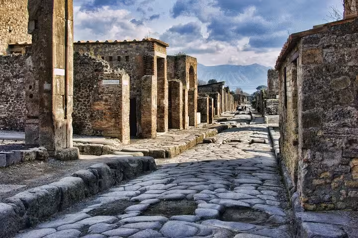Walk along the historic stone streets of Pompeii, showcasing well-preserved ruins and distant mountain views.