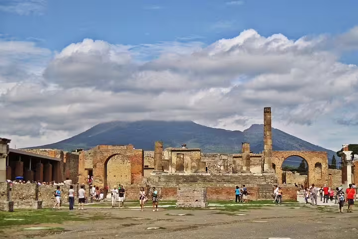 Tourists exploring ancient Pompeii ruins with Mount Vesuvius backdrop on a private full-day driver tour from Naples