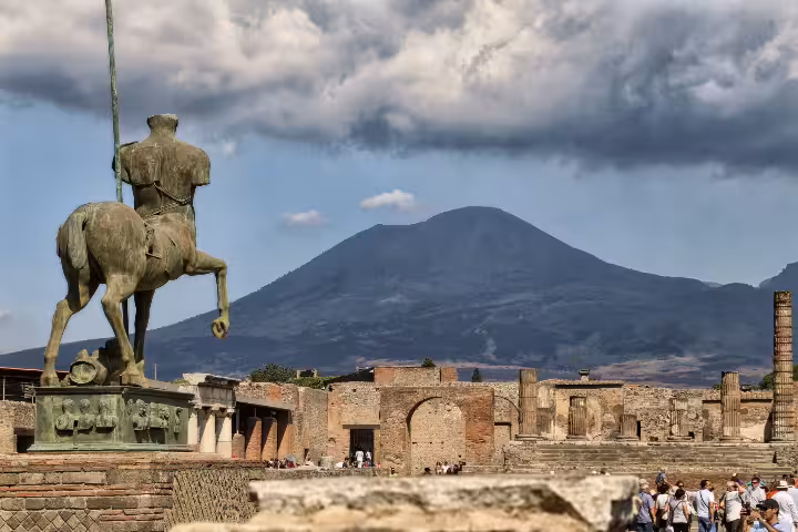 Pompeii ruins with Mount Vesuvius backdrop and statue, highlight stop on Pompeii and Vesuvius tour from Naples