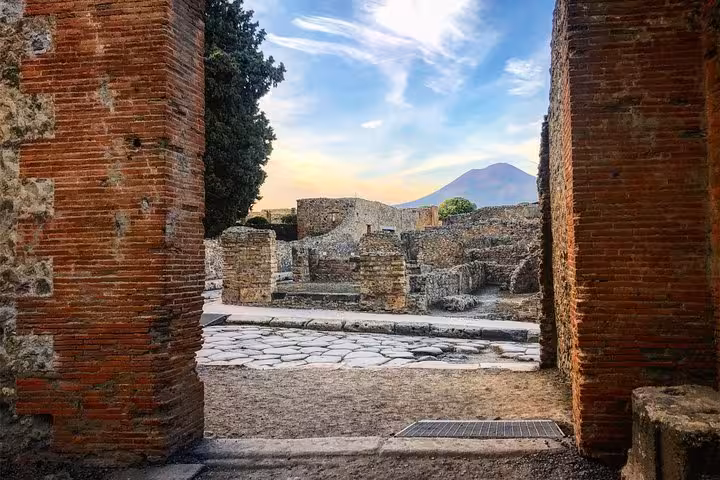 View of Pompeii ruins framed by ancient brick walls with Mount Vesuvius in the background at sunset.