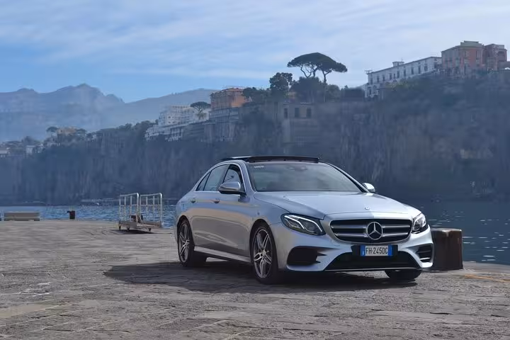 Luxury car parked by the scenic Positano coastline, offering comfortable transfer for the Pompeii guided tour.
