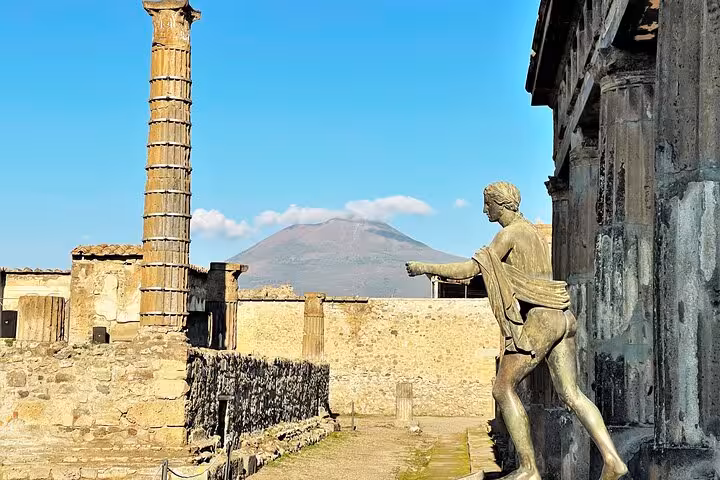 Statue and ancient columns with Mount Vesuvius in the background, highlighting Pompeii's historical allure.