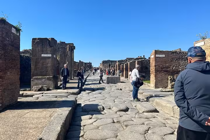 Tourists exploring ancient streets of Pompeii under a clear blue sky, highlighting the historical allure of the ruins.