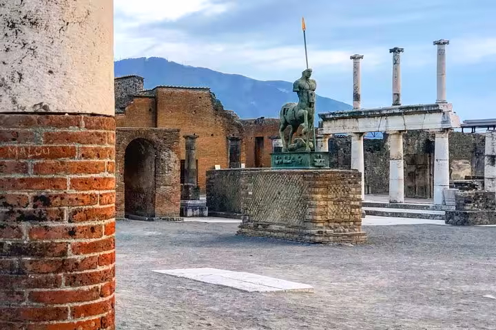 Majestic statue and ancient columns at Pompeii with Mount Vesuvius visible, showcasing historic allure and scenic beauty.