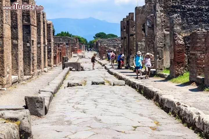Visitors walking along an ancient stone street in Pompeii with Mount Vesuvius in the distance on a guided shore excursion
