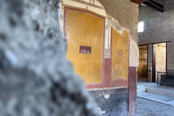 Ancient frescoes with vibrant yellow and red hues in a Pompeii ruin, showcasing historic Roman artistry.
