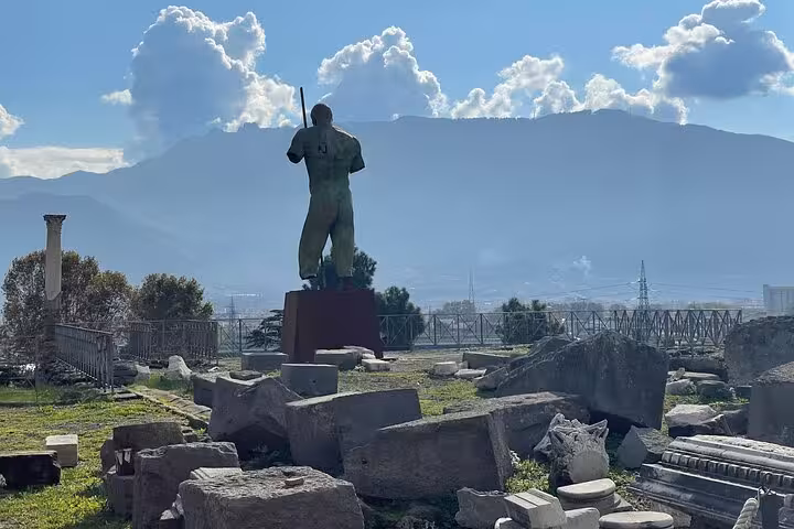 A statue overlooks the ruins of Pompeii with Mount Vesuvius in the background, highlighting the historical tour's scenic views.