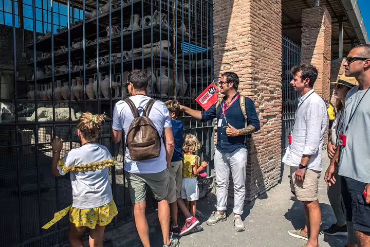 Visitors observe artifacts and pottery at an excavation site during the guided Pompeii tour, showcasing historical insights.