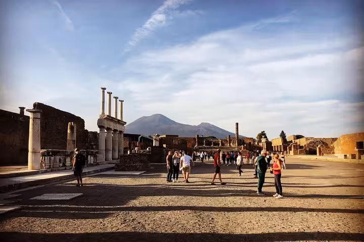Visitors explore Pompeii's historic ruins with Mount Vesuvius as a stunning backdrop during a tour from Positano.