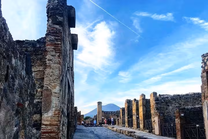 Explore the ancient streets of Pompeii with a view of Mount Vesuvius under a bright blue sky, perfect for history enthusiasts.