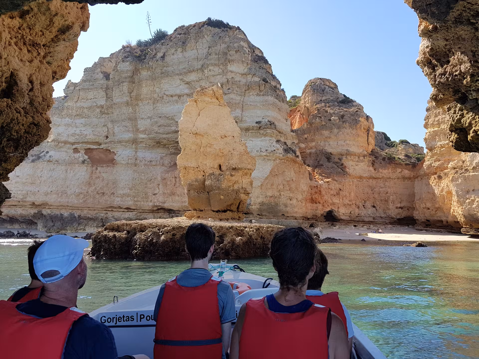Visitors on a Lagos grotto boat tour approach golden Ponta da Piedade cliffs and secluded Algarve beach in clear turquoise water