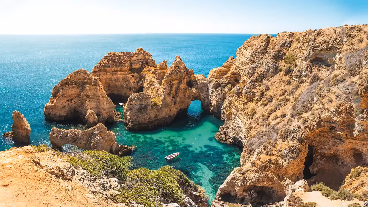 Stunning Ponta da Piedade rock arches and sea caves with a skiff boat exploring crystal-clear turquoise waters in Lagos