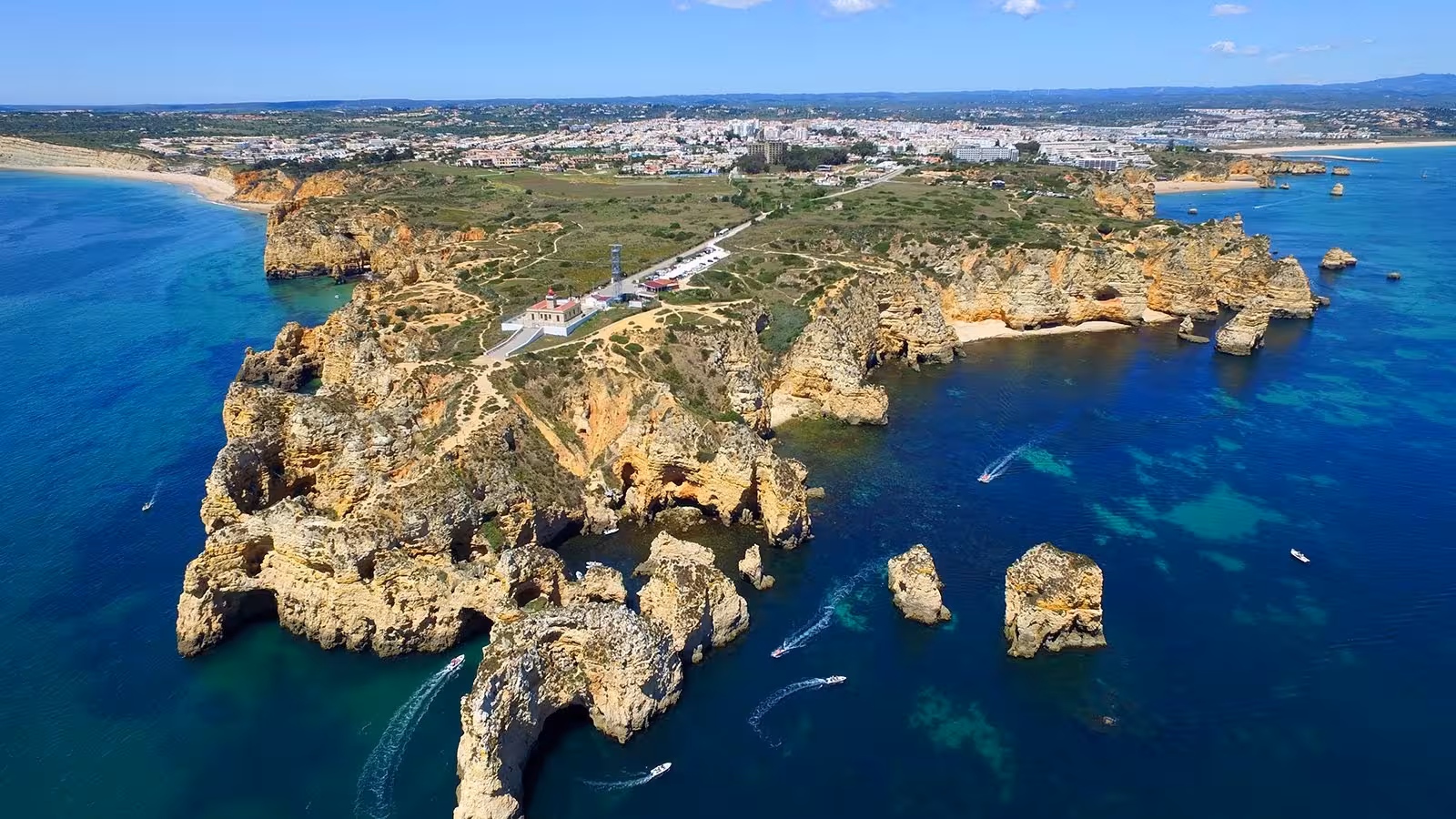 Aerial view of Ponta da Piedade rock formations, lighthouse and boats cruising the crystal-blue Algarve coast near Lagos