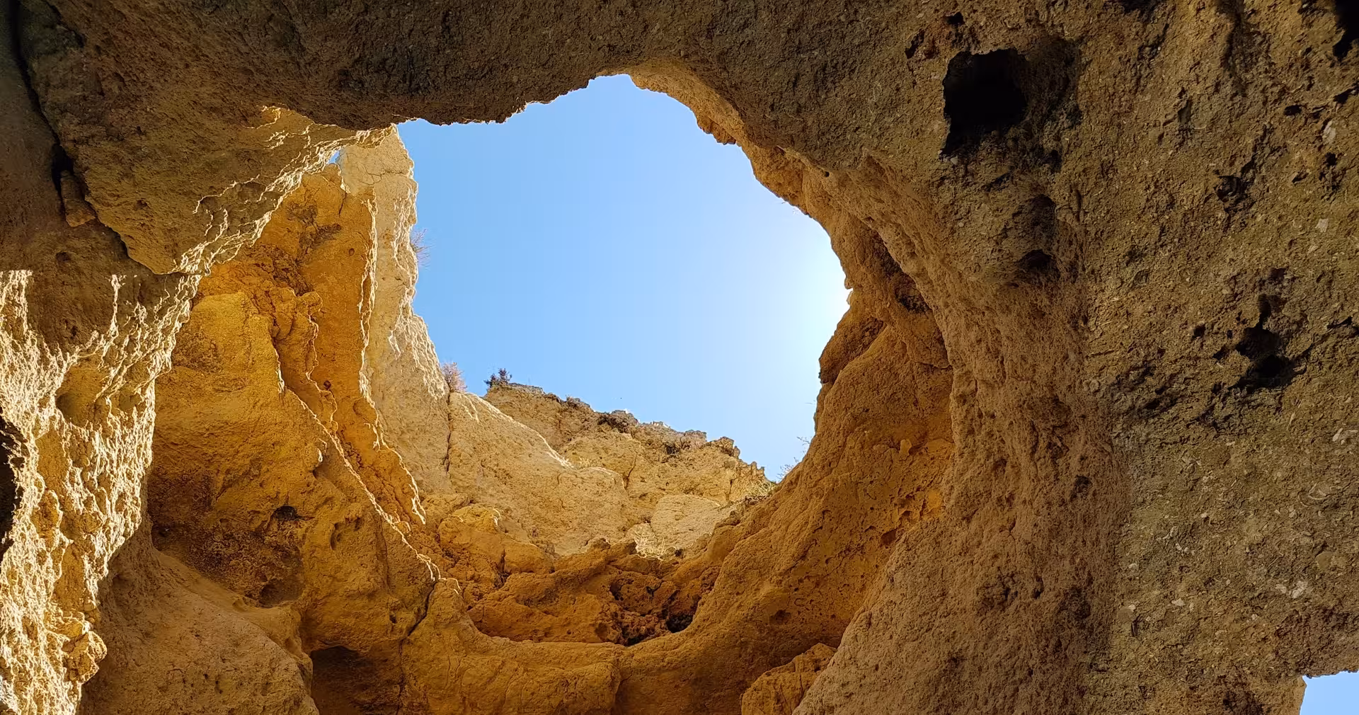 View from inside a natural rock chimney at Ponta da Piedade, Lagos, framing the clear blue Algarve sky above