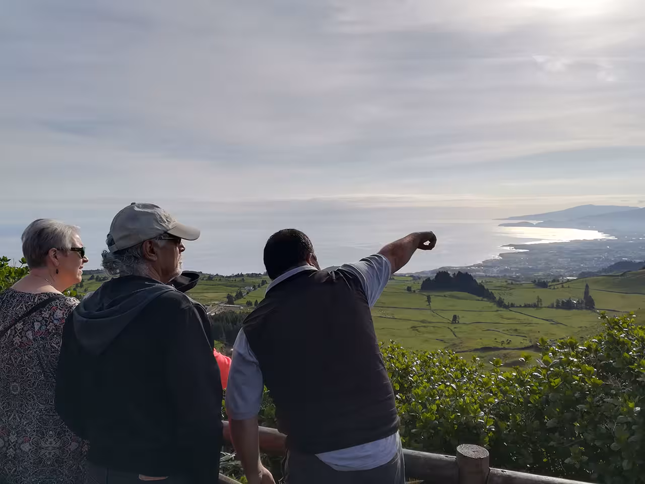 Guide pointing out coastal views over green pastures on a full day private 4x4 tour from Ponta Delgada, São Miguel Island