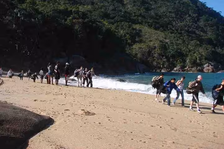 Group of tourists walking along the sandy beach of Ponta Negra with lush forest backdrop and ocean waves.