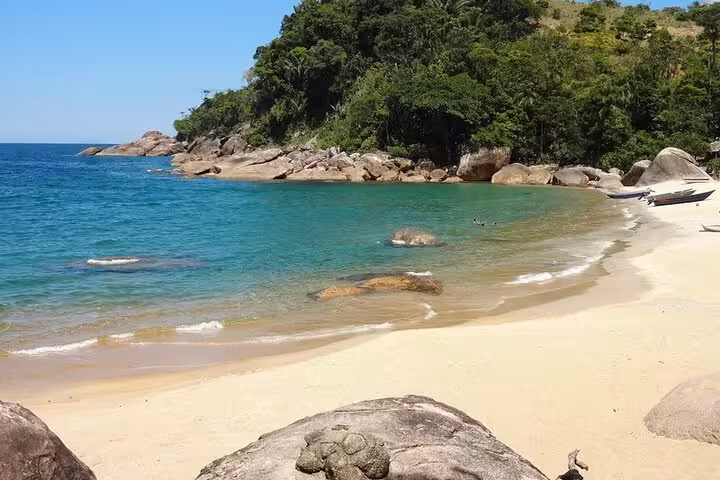 Scenic view of Ponta Negra's tranquil beach with turquoise waters, rocky shoreline, and lush green hills.