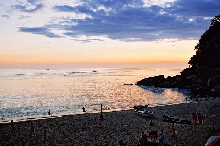 Sunset view at Ponta Negra beach with people enjoying the serene ocean, boats, and a vibrant evening sky.