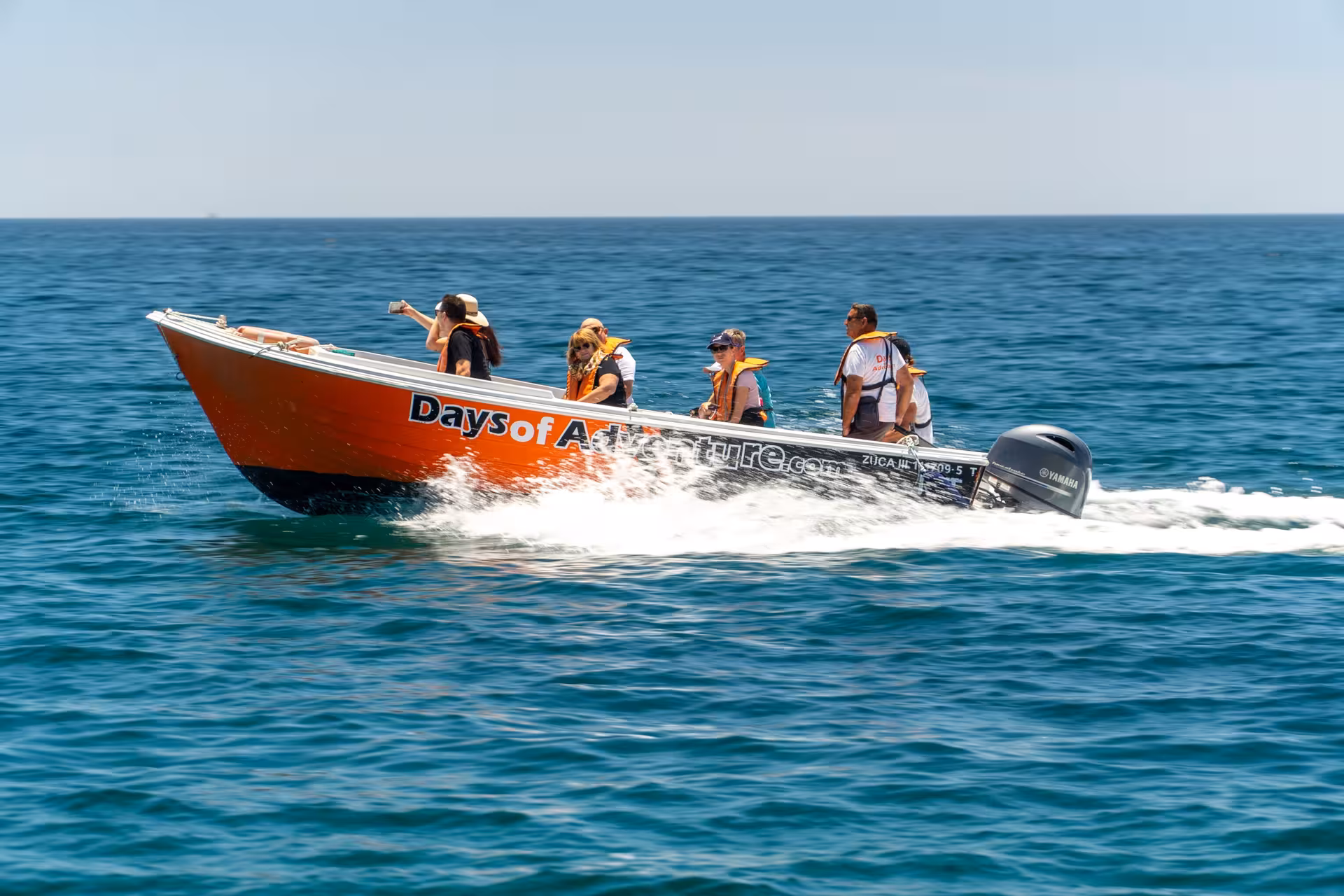 Tourists wearing life jackets on an orange Days of Adventure speedboat cruising the Algarve sea on a Ponta da Piedade cave tour