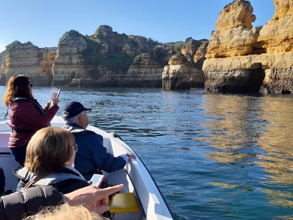 Tourists photograph dramatic sea cliffs and crystal-clear water from a small boat on the Ponta da Piedade grotto tour in Lagos
