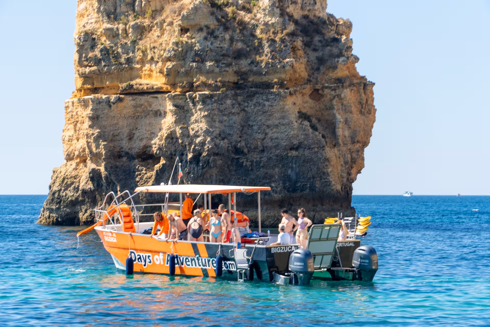 Adventure boat anchored near dramatic limestone sea stacks at Ponta da Piedade, Lagos, Algarve, with tourists ready to kayak.