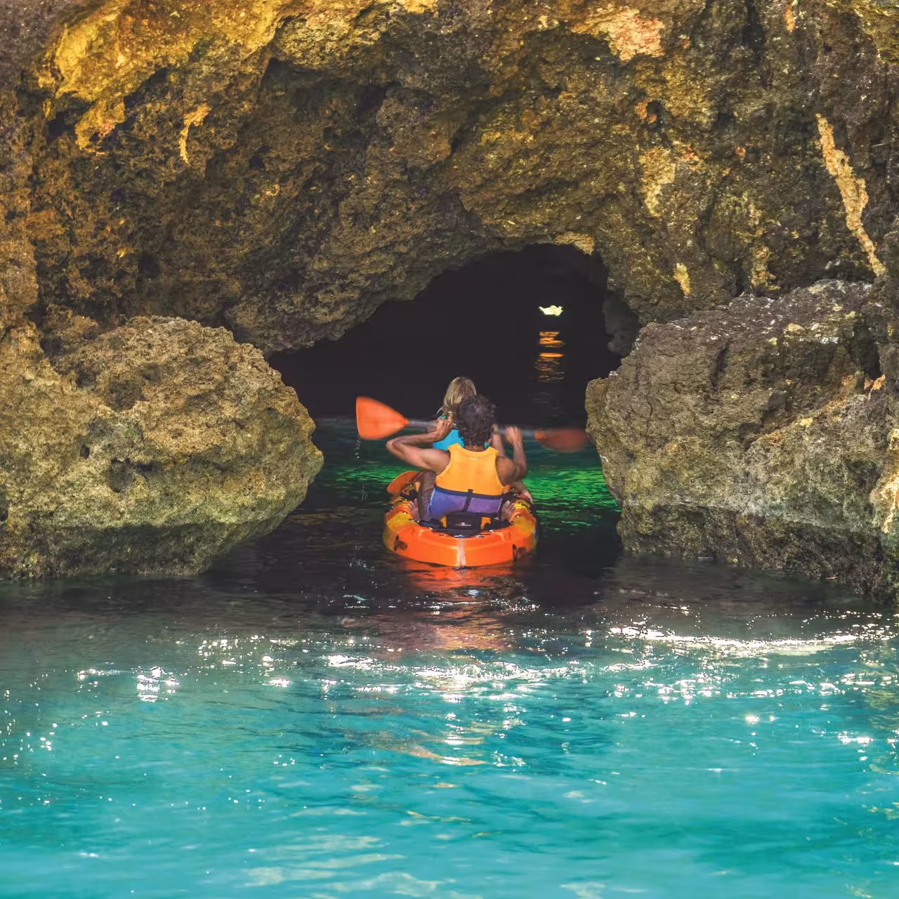 Two kayakers paddling through a stunning sea cave on a Lagos kayak experience in turquoise Algarve waters