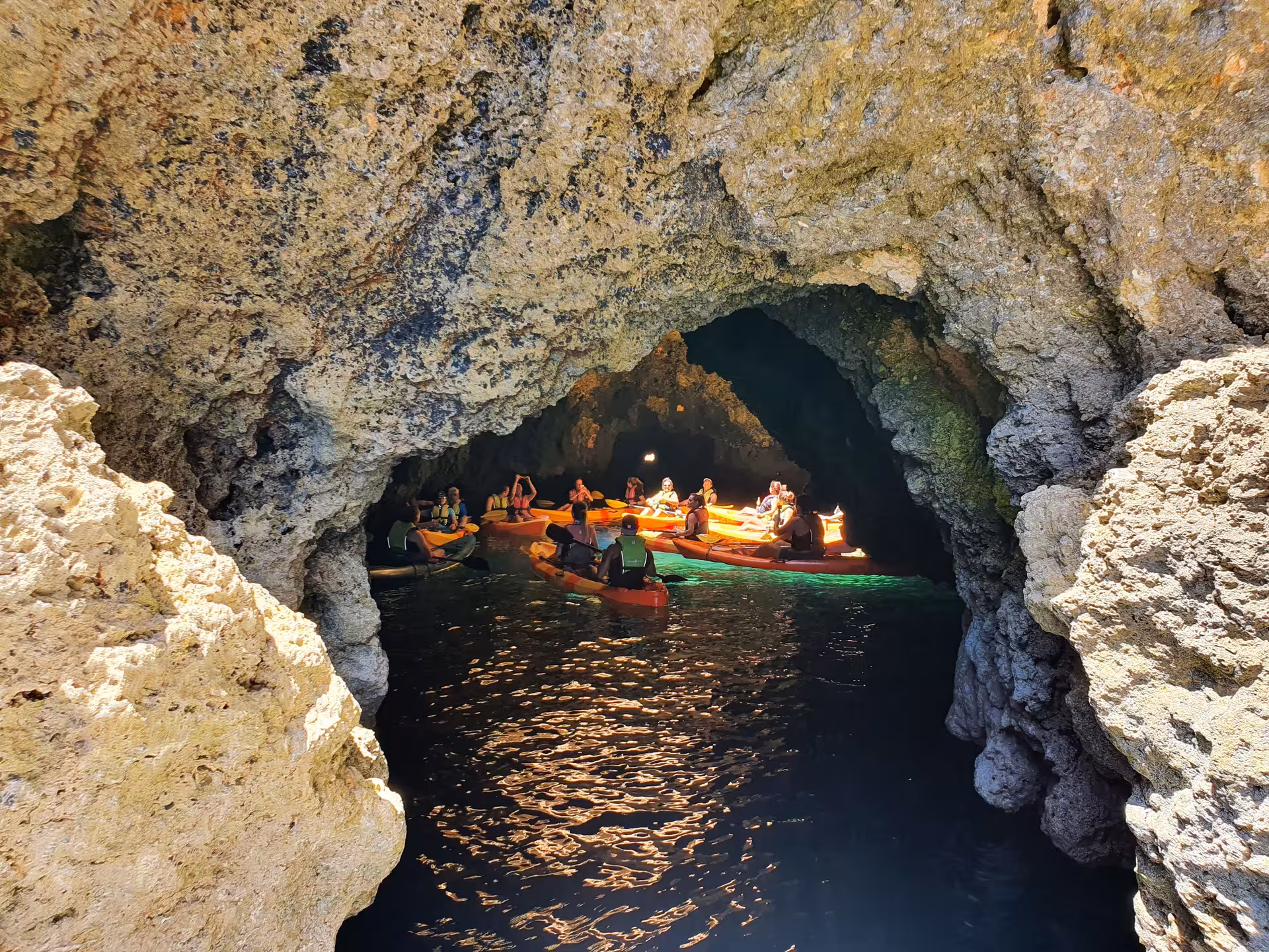 Kayak tour group exploring a dramatic sea cave at Ponta da Piedade with glowing lights reflecting on dark water in Algarve