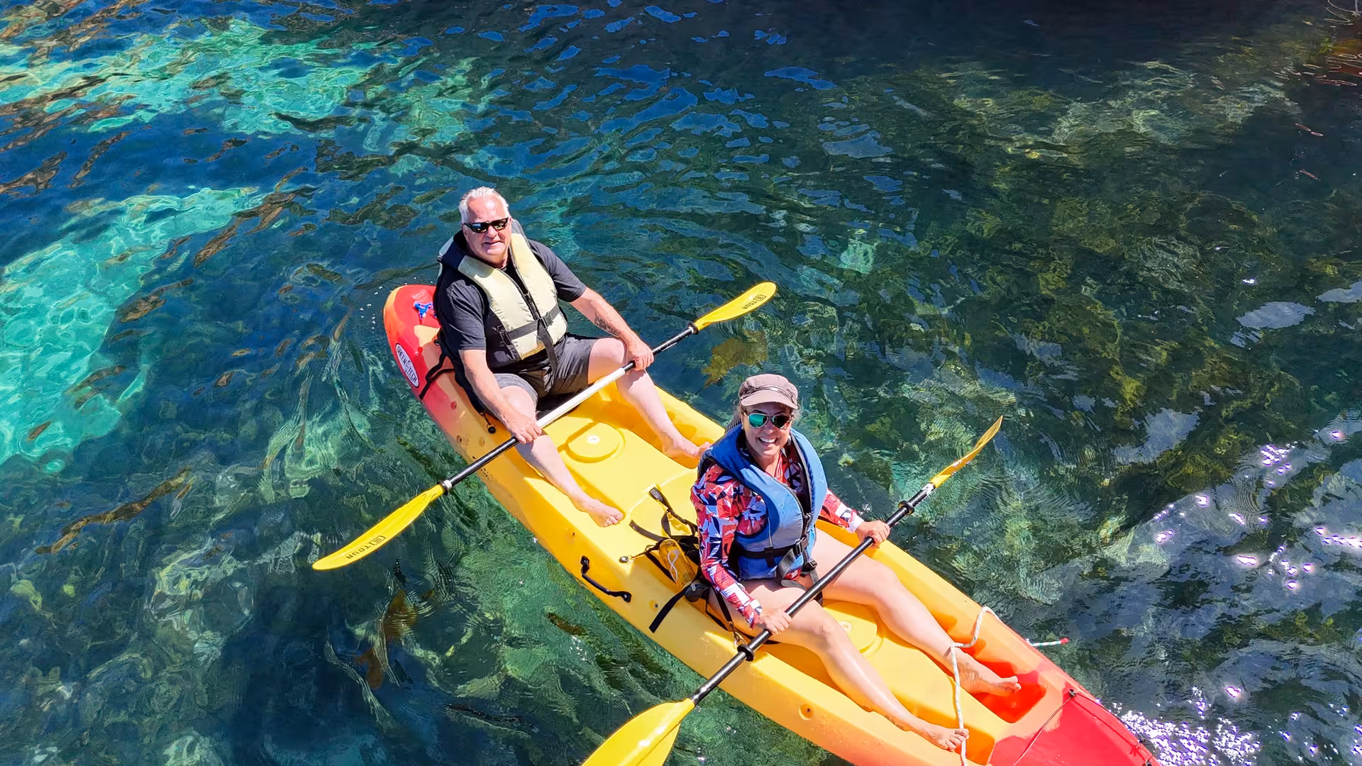 Couple paddling a yellow tandem kayak over crystal-clear turquoise waters on a Ponta da Piedade kayak tour in Lagos, Algarve.