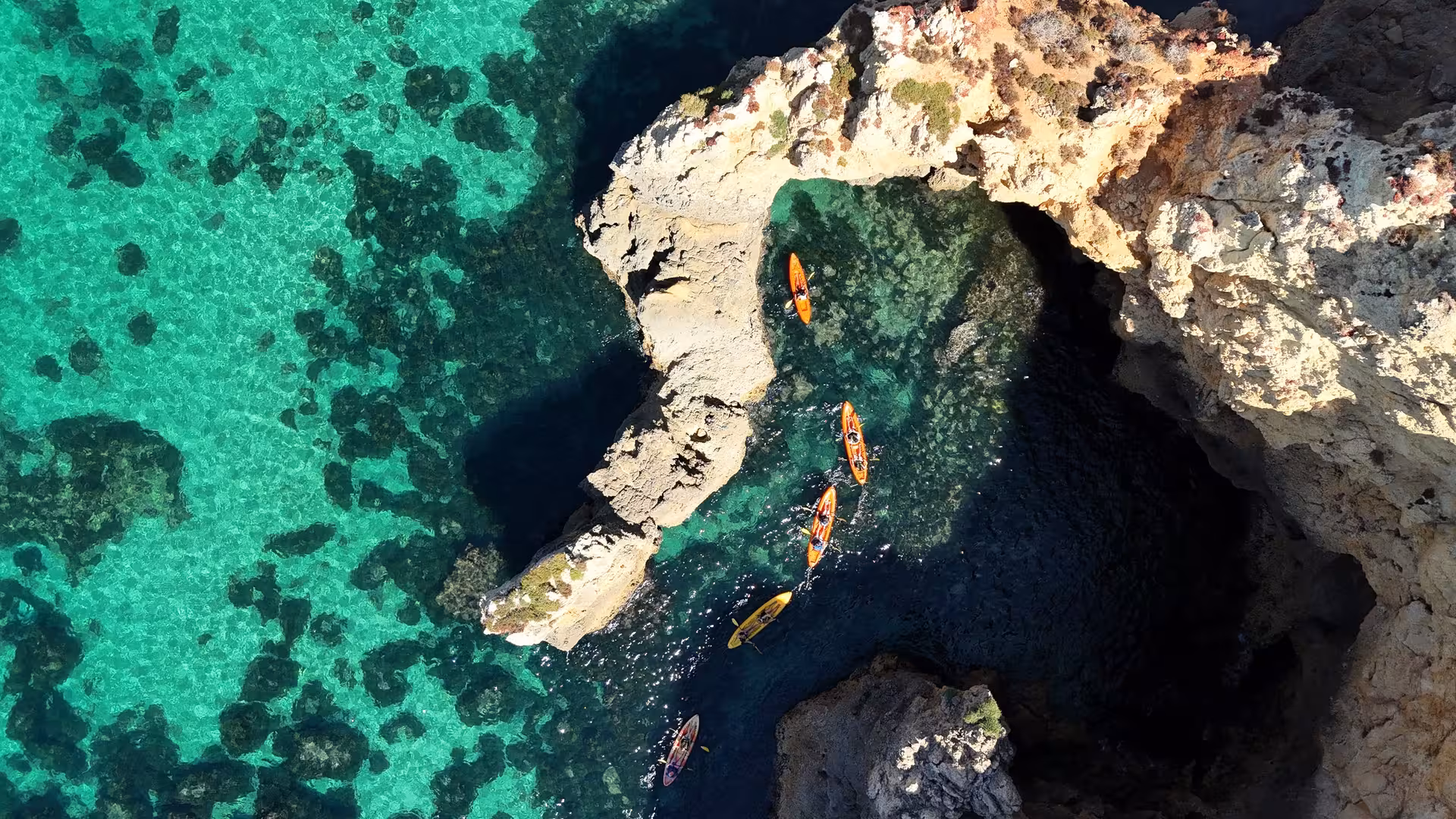 Aerial view of colorful kayaks navigating crystal-clear turquoise waters through stunning rock formations at Ponta da Piedade Lagos Algarve