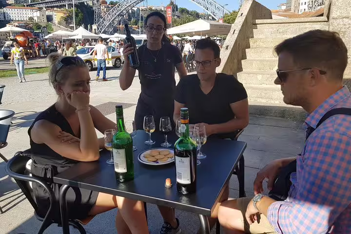 Outdoor wine tasting by the Douro River with visitors enjoying Port wine and snacks on a sunny day.