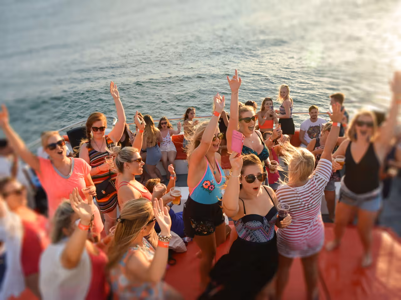 Excited crowd dancing and raising hands on a Portimao boat party cruise under golden sunset light.