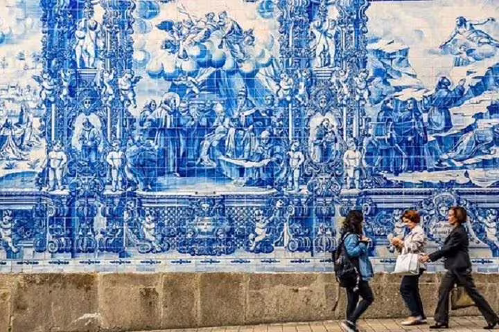 Tourists admire intricate blue azulejo tiles on a historic building in Porto, perfect for a cultural walking tour.