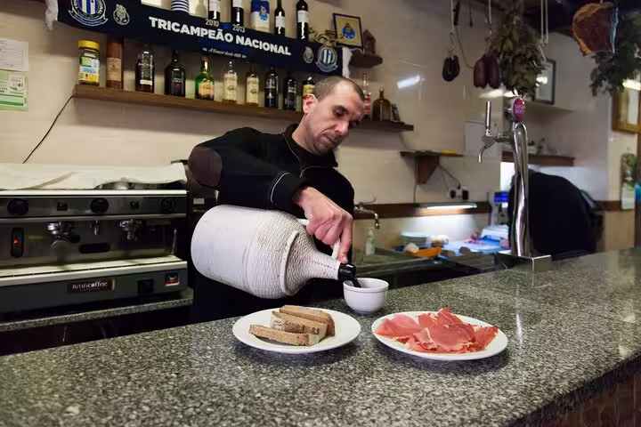 Bartender in Porto pouring wine with plates of ham and bread, showcasing local flavors on the Porto food tour.