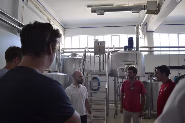 Group of people touring a Porto brewery, standing near large stainless steel brewing tanks and machinery.